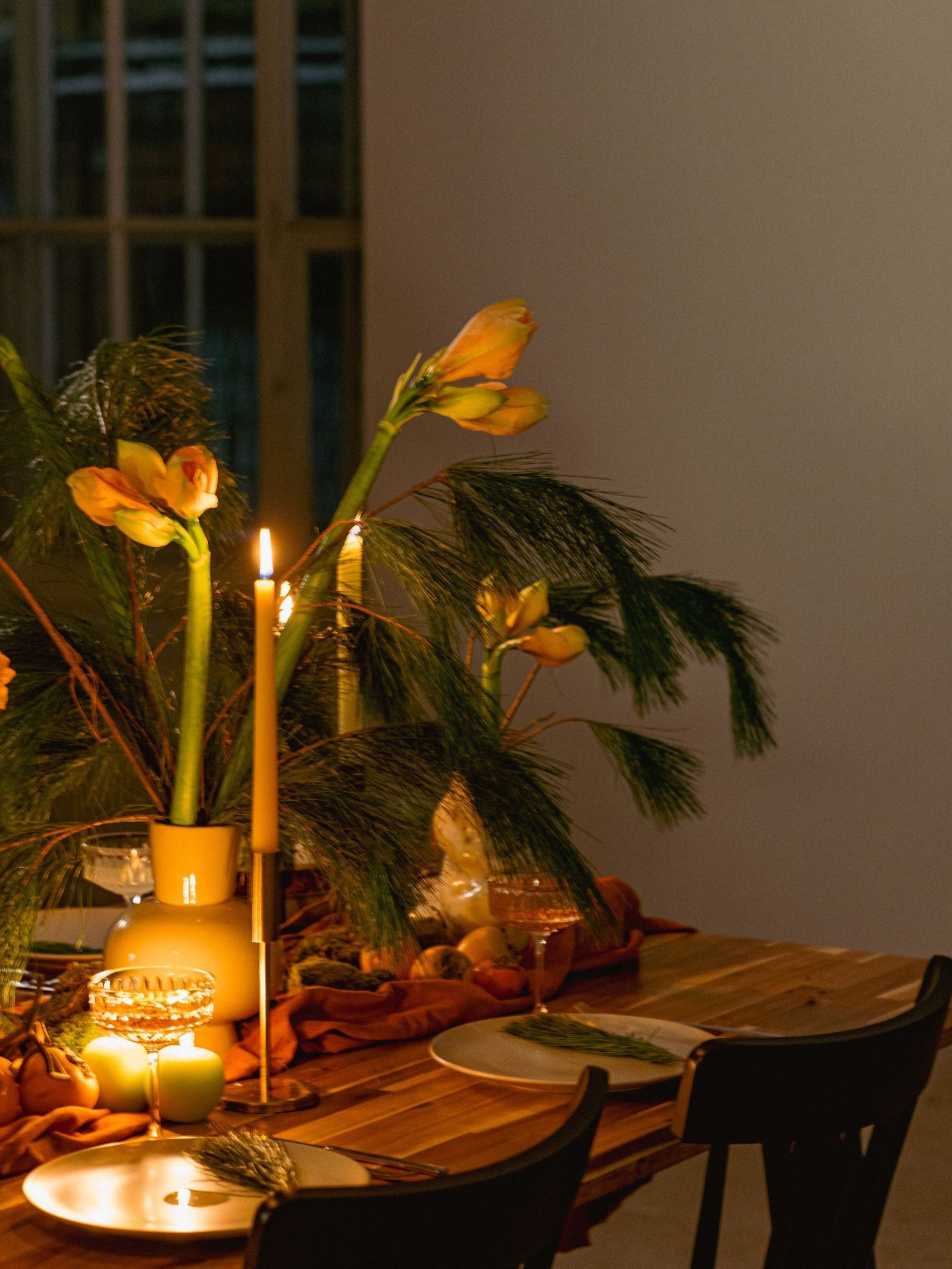 A candlelit table with yellow tulips and greenery, ready for guests