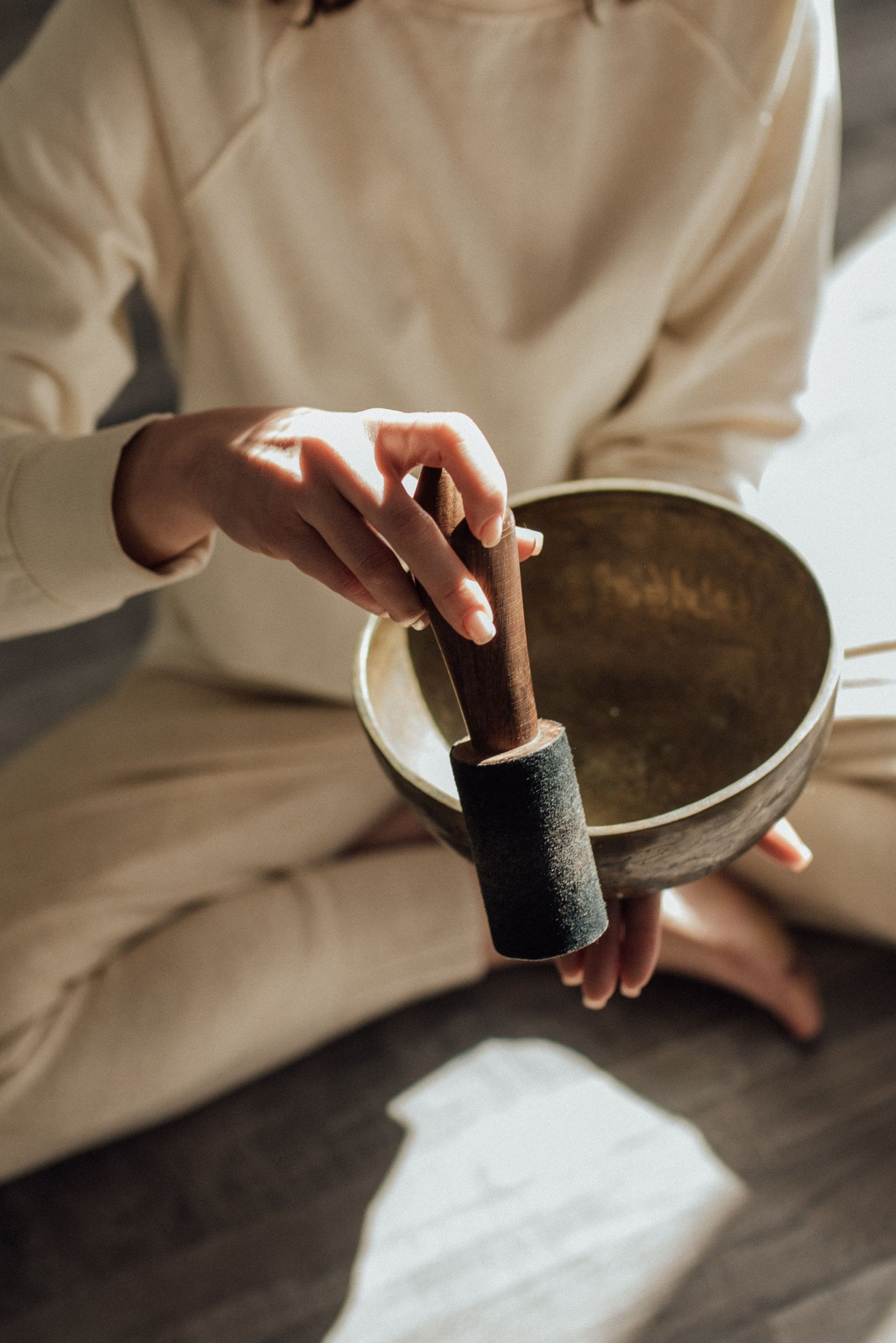 A practitioner in cream linen holding a brass singing bowl and mallet