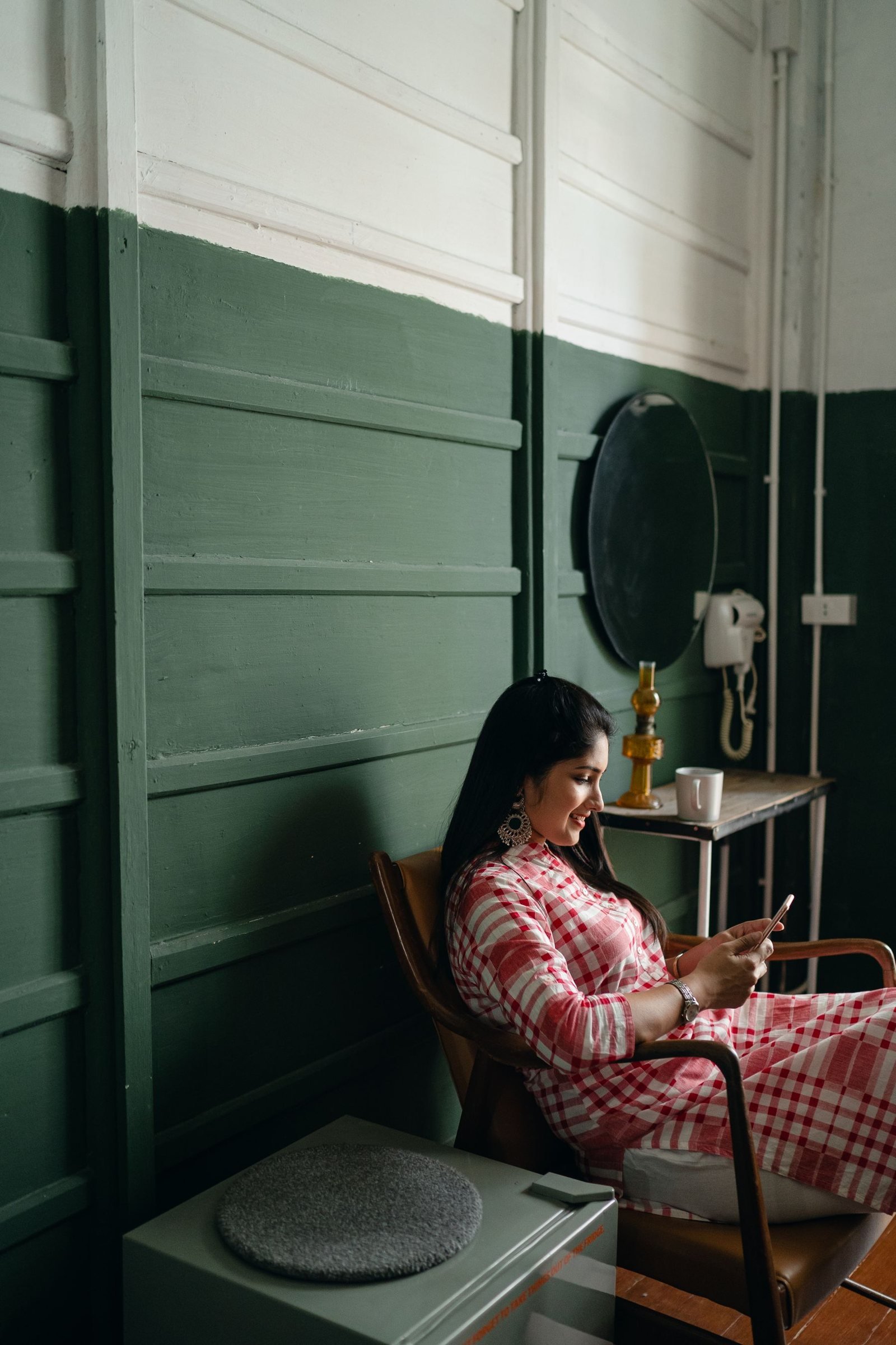 A woman browsing her phone in a calm room with a sage-green wall