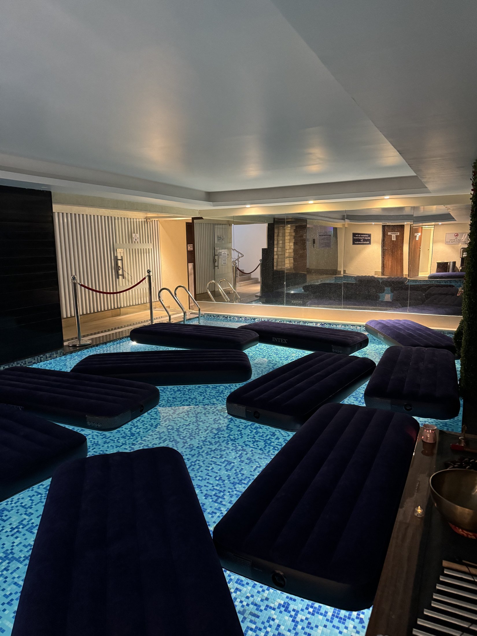 Floating beds arranged across a softly lit indoor pool, ready for guests