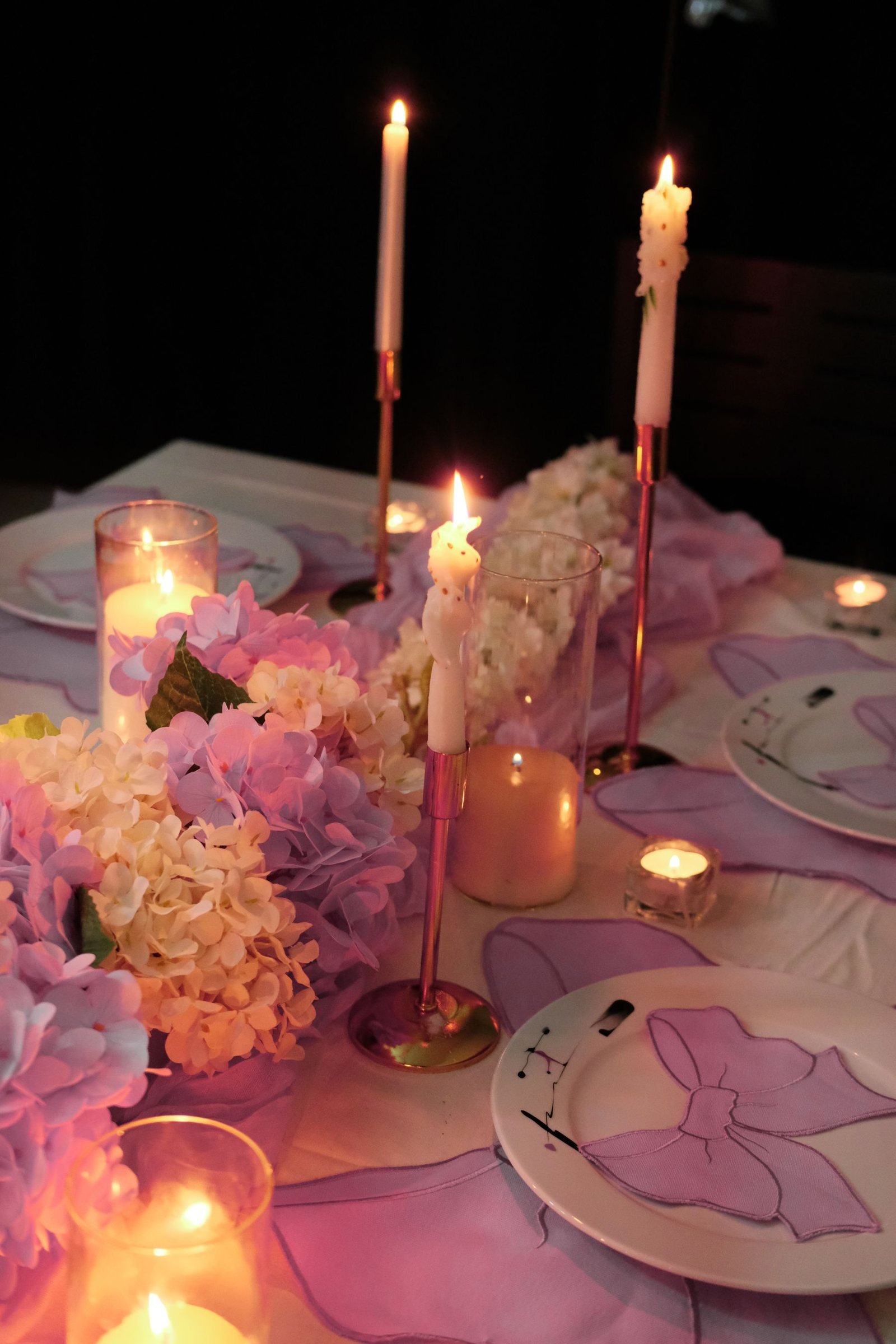 A celebration table with tall candles, pink flowers and glowing votives