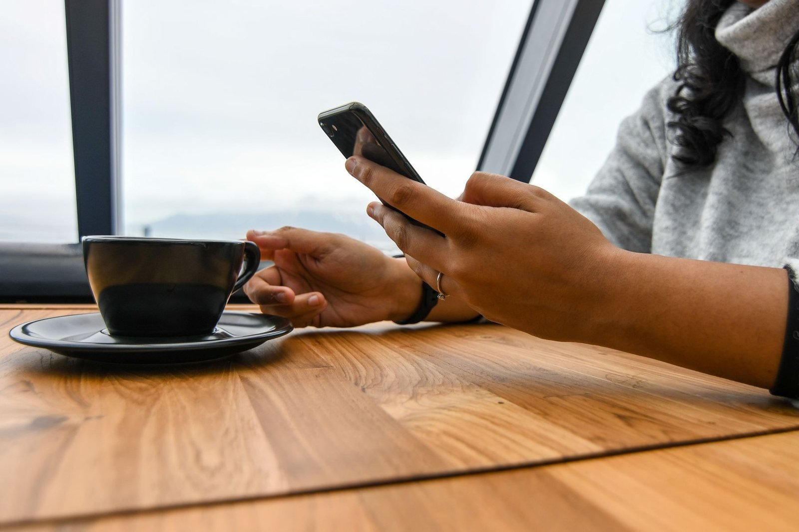 Hands sending a message on a phone beside a cup of coffee