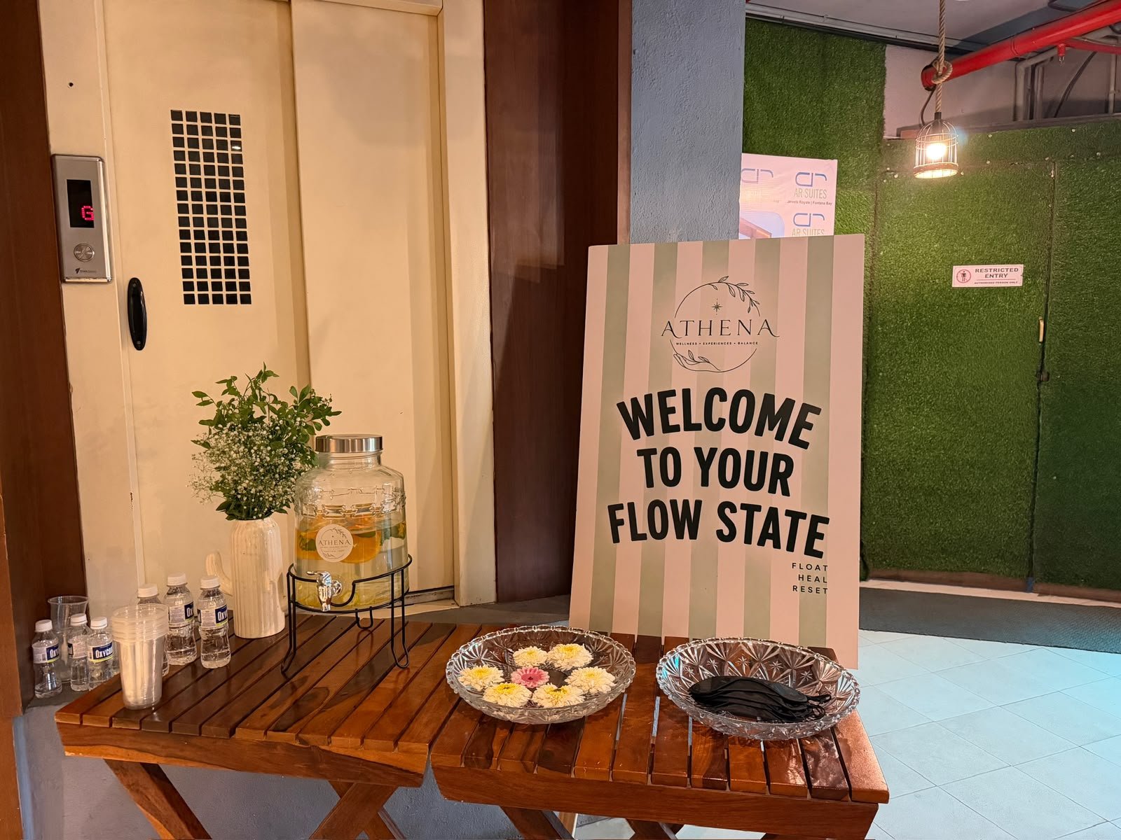 A welcome table with infused water, flowers and eye masks beside an Athena sign reading Welcome to your flow state